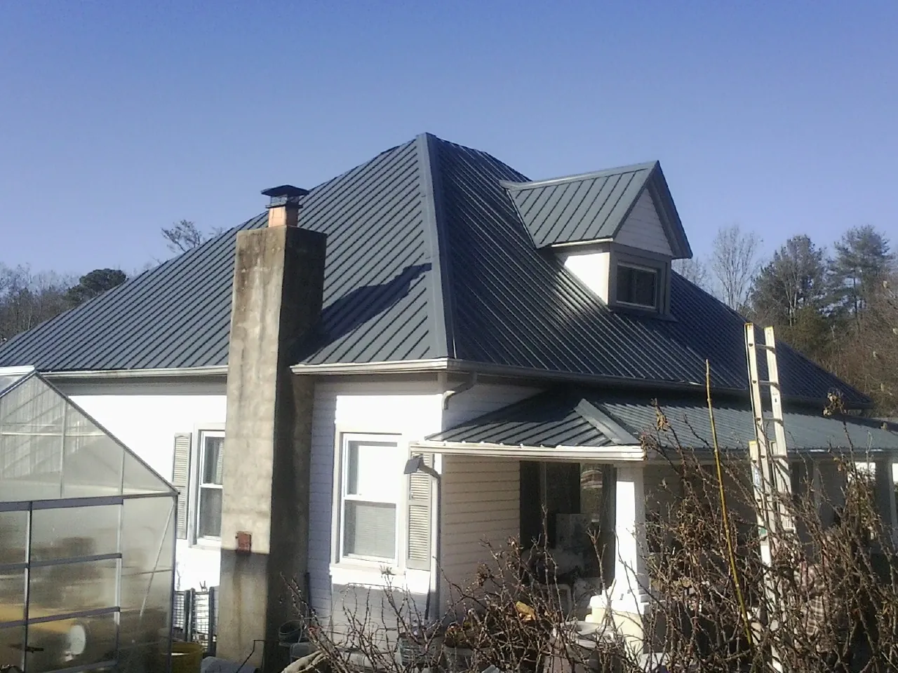 Dark blue standing seam metal roof on a white farmhouse with dormer — Slate & Tile Roof Repair by Roofing Brothers in Hanford