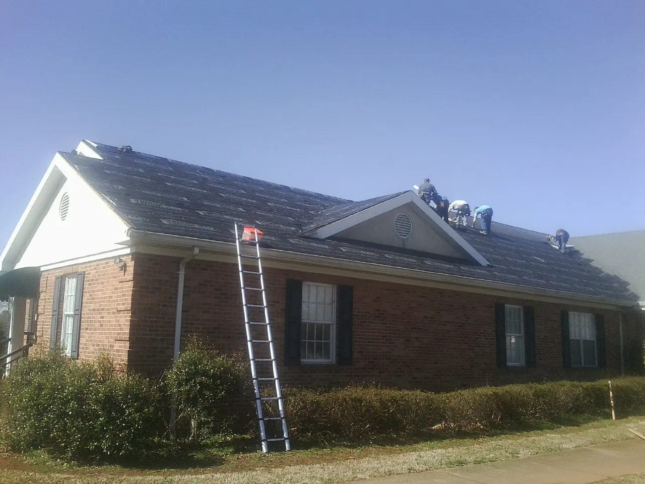 Crew tearing shingles off a brick ranch roof with a ladder set — Metal Roof Repair work by our crew in Hanford