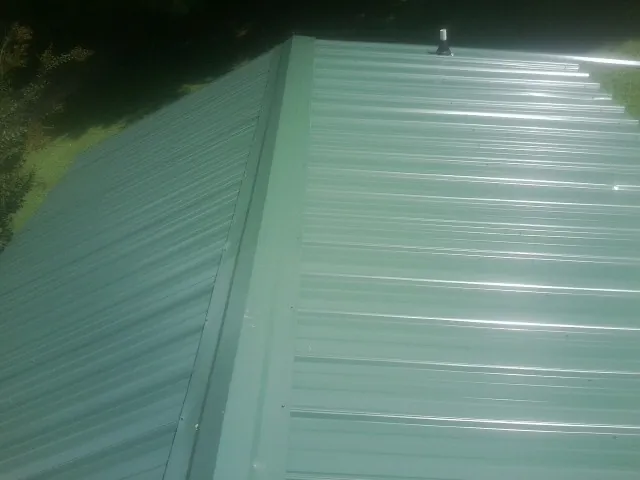 New green metal panels meeting at the ridge of a roof — Flat Roof Repair work by our crew in Hanford