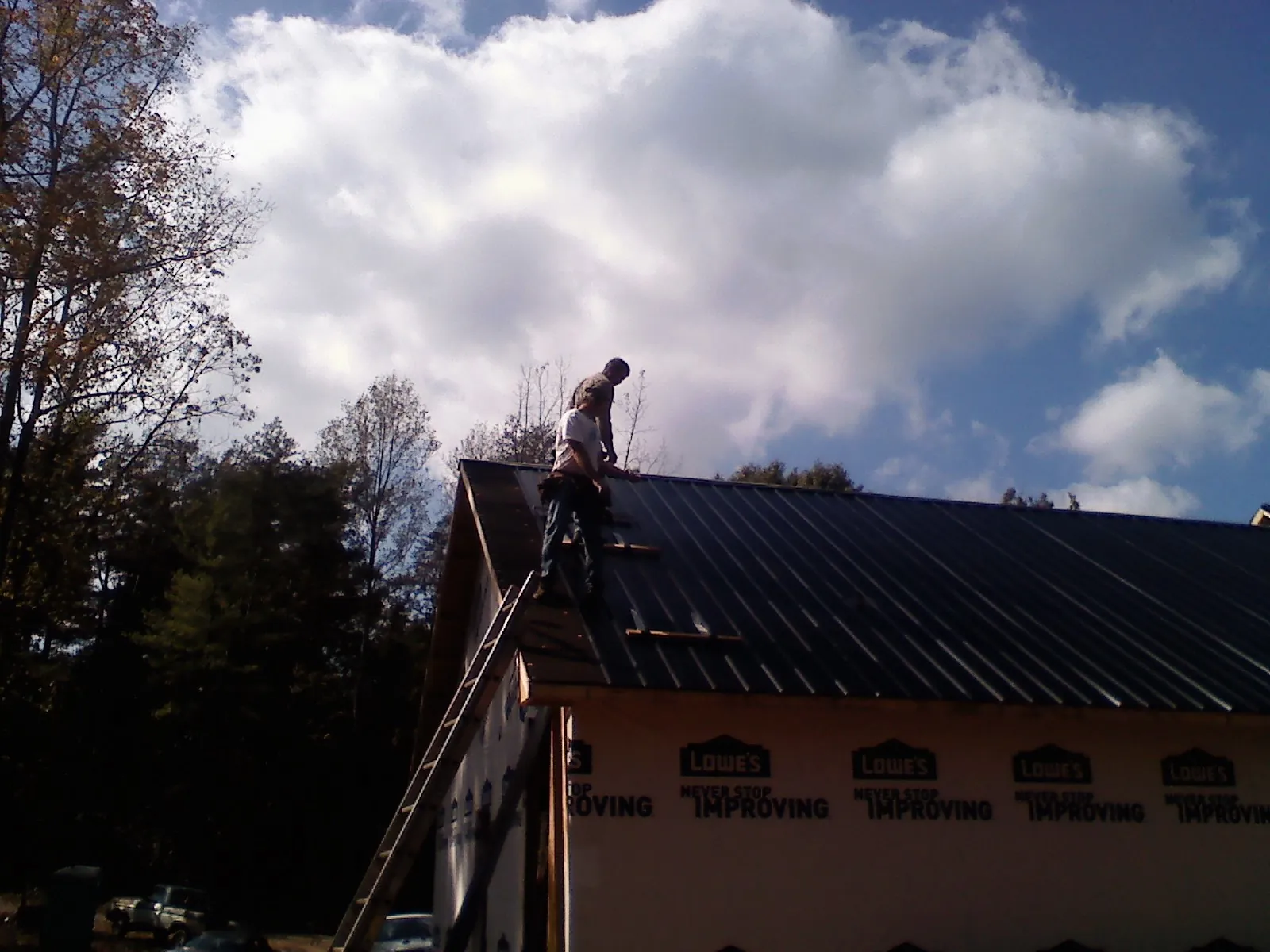 Roofer fastening dark metal panels high against a cloudy sky, from a Roof Inspection job in Hanford