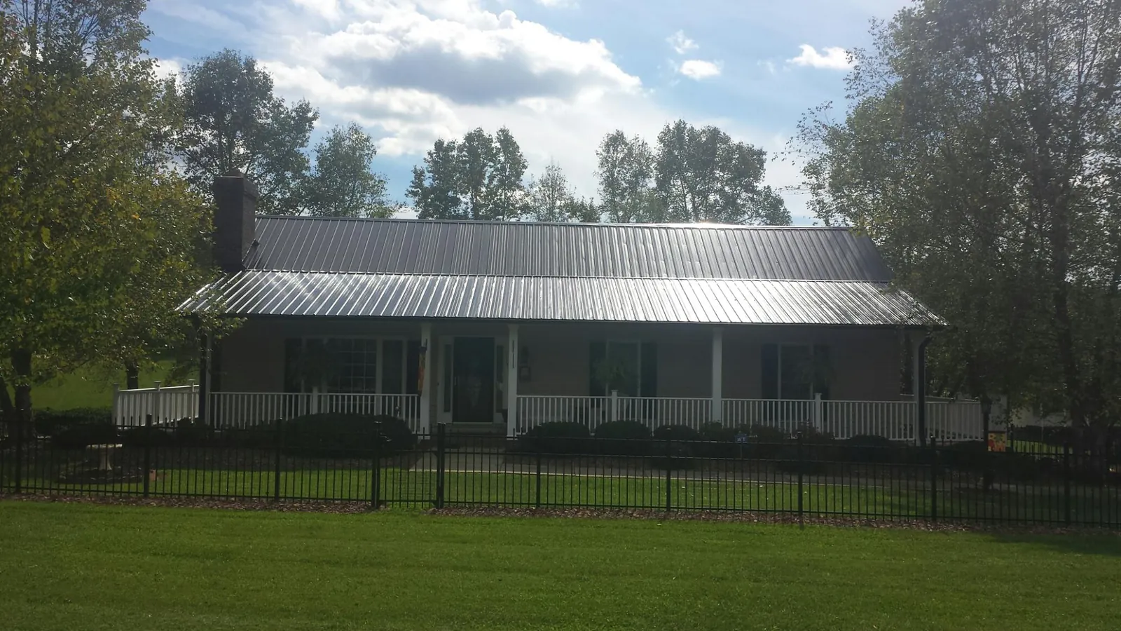 Gray metal roof on a brick ranch with a full width front porch — Gutter Guard Installation work by our crew in Hanford