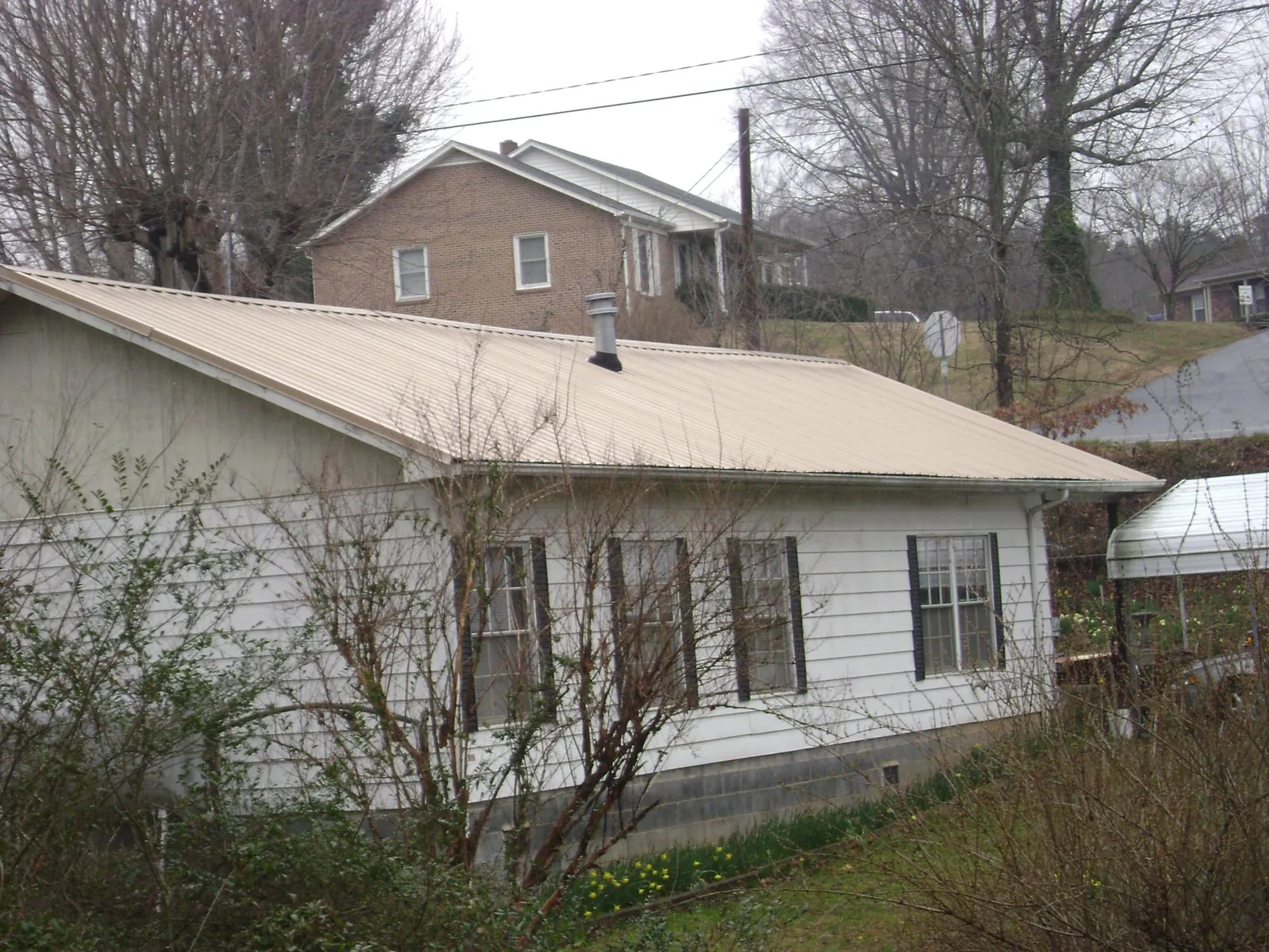 Tan metal roof on a white sided house set into a hillside — Commercial Roofing by Roofing Brothers in Hanford